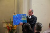 Pfarrer Dr. Joram Luttenberger freute sich sichtlich über das Geschenk des Kindergartens und präsentierte das Bild fröhlich der Festgemeinde. Foto: Jürgen Bosenius / kklios.de